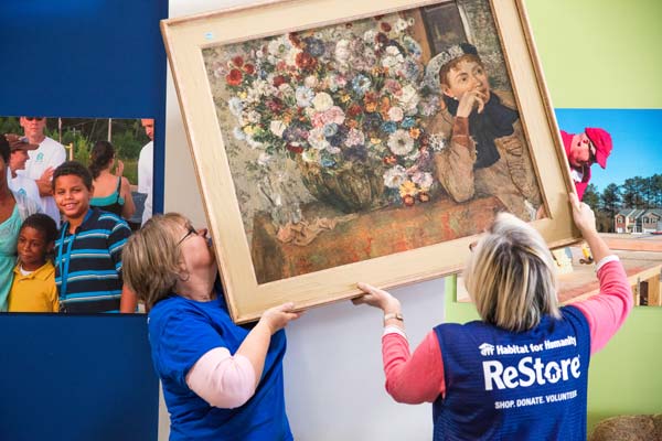 Two Habitat ReStore volunteers hanging a piece of art