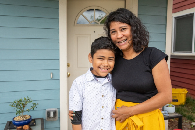 A mother and son smiling in front of their Habitat home