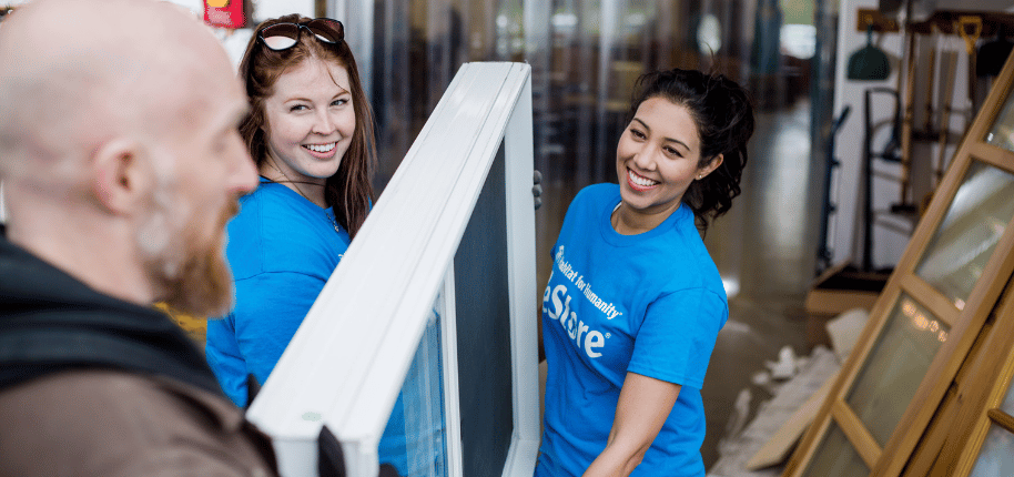 A man hands off a window to two women volutneering at a Habitat for Humanity ReStore